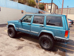 1999 Jeep Cherokee 4x4 with new lift kit and all-terrain tires, parked in a lot, showcasing its rugged design.